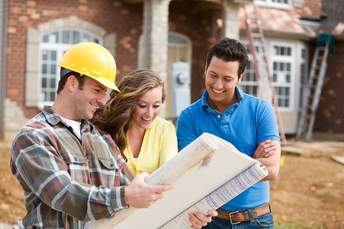 A construction worker reviewing home blueprints with homeowners