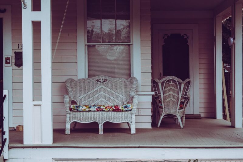 Wicker sofa sitting on a front porch of an older home.