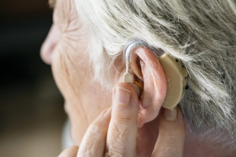 A person with grey hair turning up the volume on a hearing aid