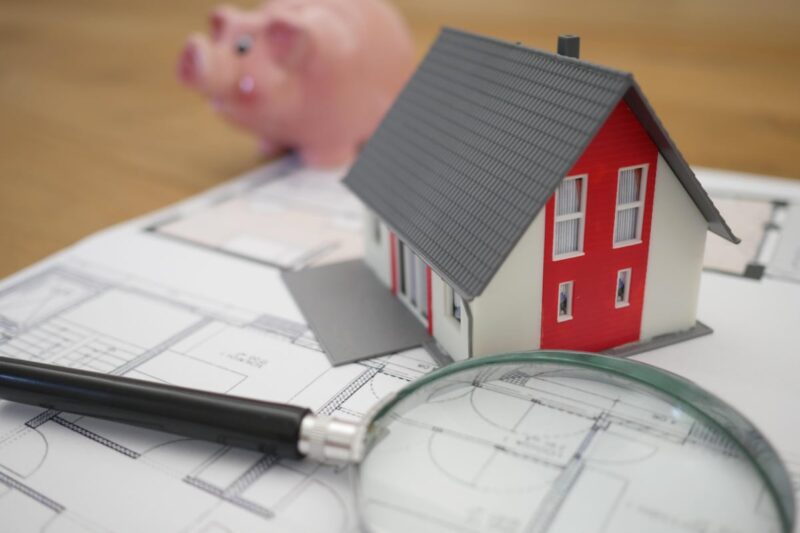 A house figurine sitting on top of a home blueprint with a magnifying glass