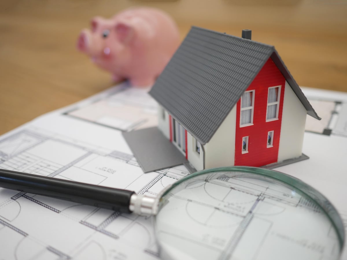 A house figurine sitting on top of a home blueprint with a magnifying glass